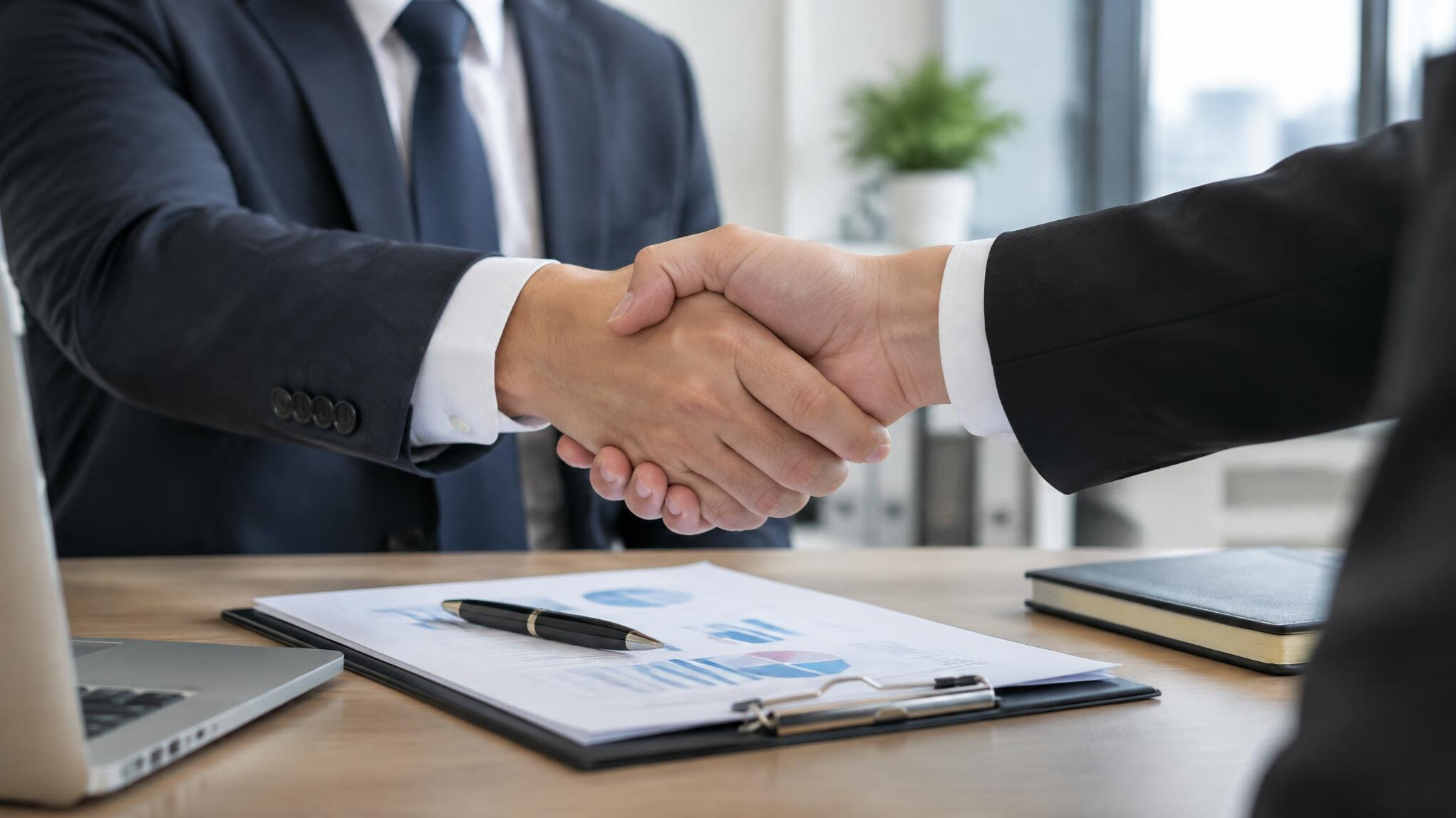 Close-up of two people shaking hands over a desk