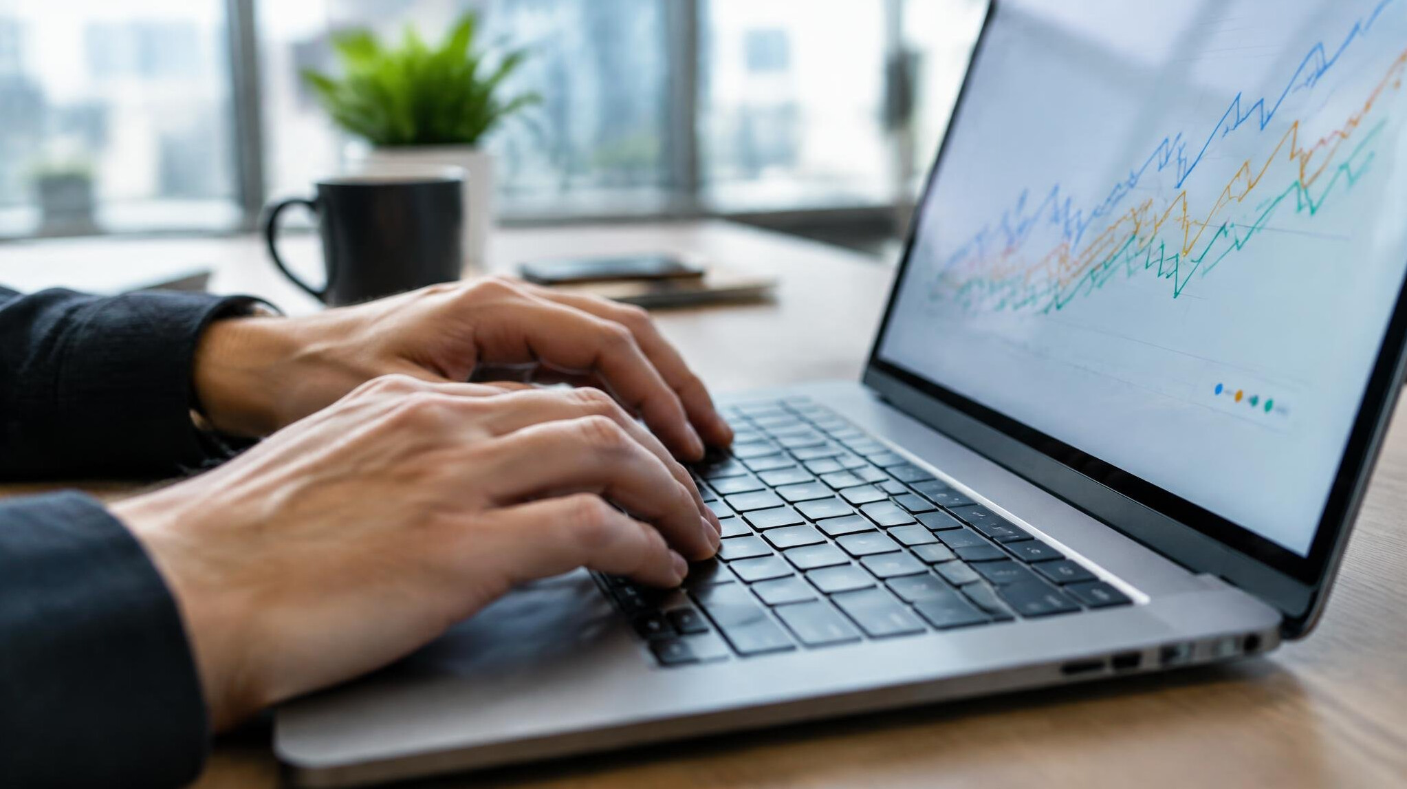 Close-up of hands typing on a laptop keyboard with charts visible on the screen